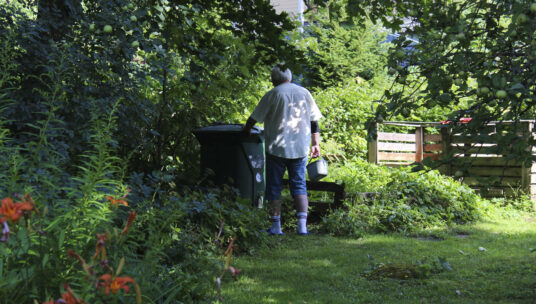 Mies on nostamassa kompostiastian kantta kukkivassa puutarhassa.